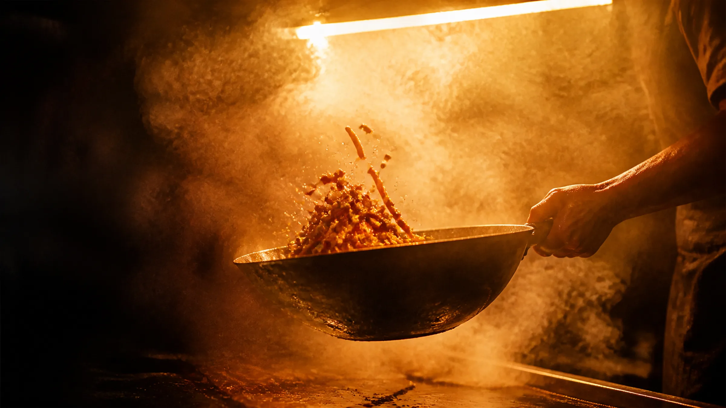 A wok under strip light with the frame two thirds full of vapour.